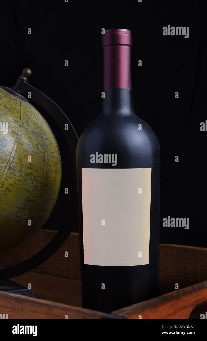 Nahaufnahme einer Rotweinflasche mit einem leeren Etikett in einer Holzkiste mit antiker Weltkugel. Stockfoto