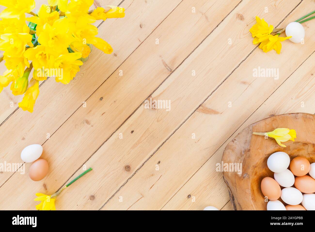 Osterhintergrund Dekoration mit Eiern in Holzschale, grünen Blättern und Osterglocken, Narzienblumen auf Holzboden. Federschmuck. Natürlich d Stockfoto