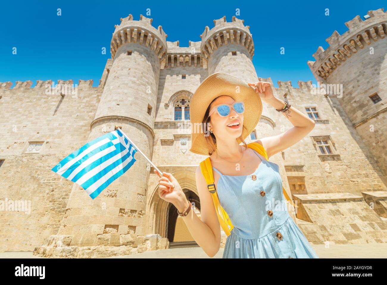 Glückliche asiatische Reisende Frau mit griechischen Flaggen mit großartigem Blick auf die alte Burg des Großmeisters der Ritter in Rhodos, Griechenland Stockfoto