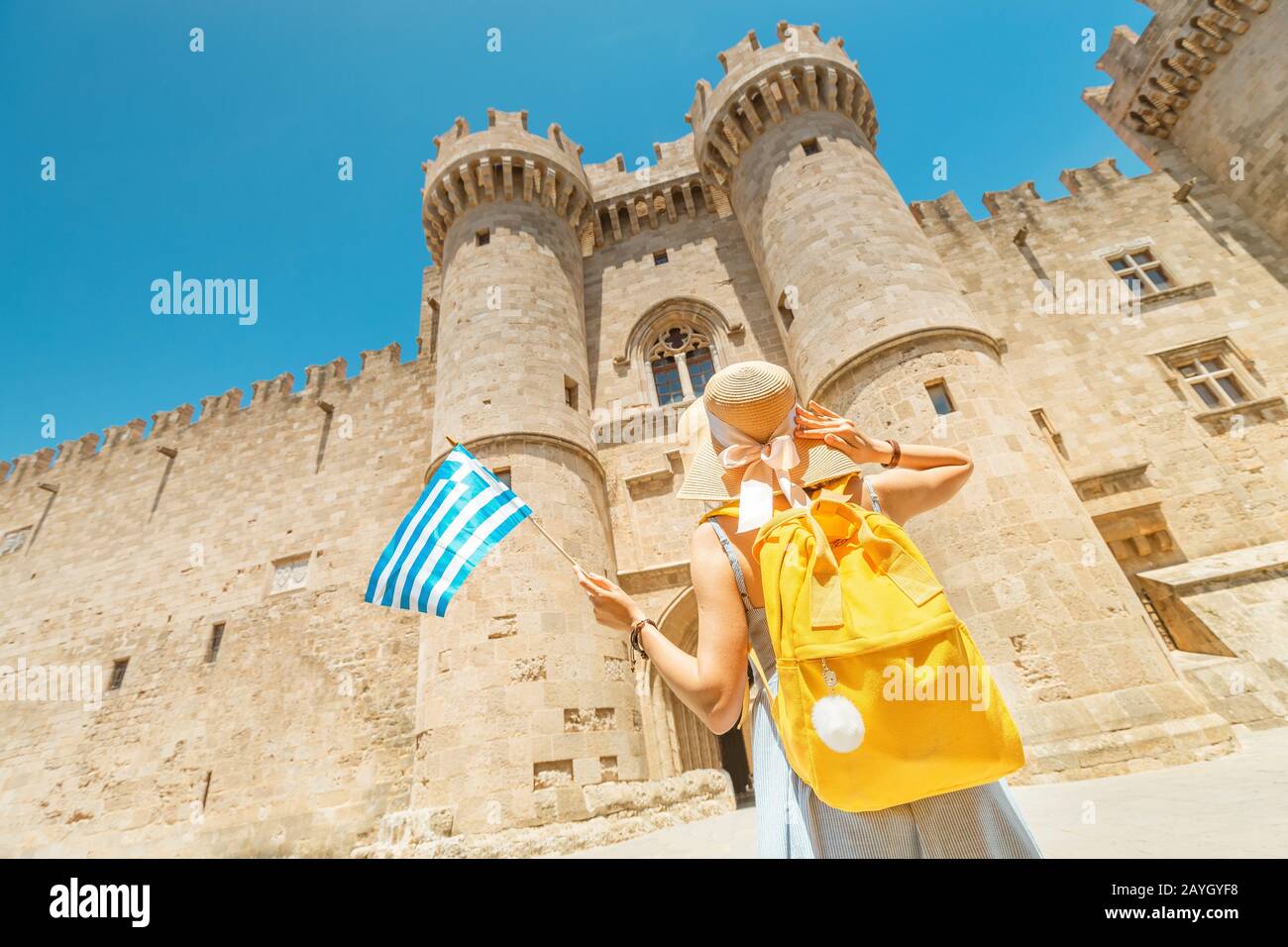 Glückliche asiatische Reisende Frau mit griechischen Flaggen mit großartigem Blick auf die alte Burg des Großmeisters der Ritter in Rhodos, Griechenland Stockfoto