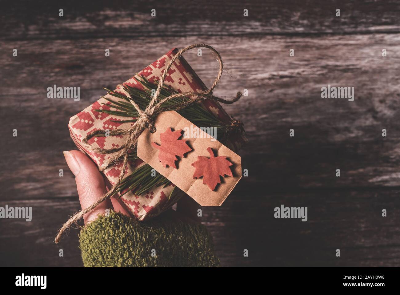 Hand mit einem kleinen geheimen Weihnachtsgeschenk mit kreativem, handgefertigtem dekorativem, rustikalen baugeschenk, das in rotem Retro-Geschenkpapier verpackt ist Stockfoto