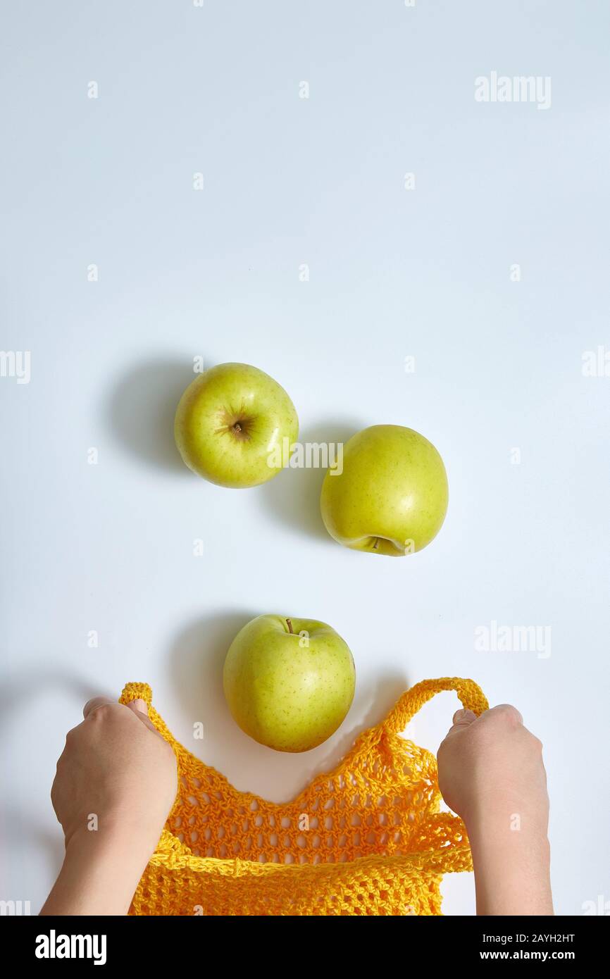 Äpfel fallen in einen offenen gelben Sack mit Netzschnur, weibliche Hände im Rahmen. Auf weißem Hintergrund mit Kopierbereich. Stockfoto