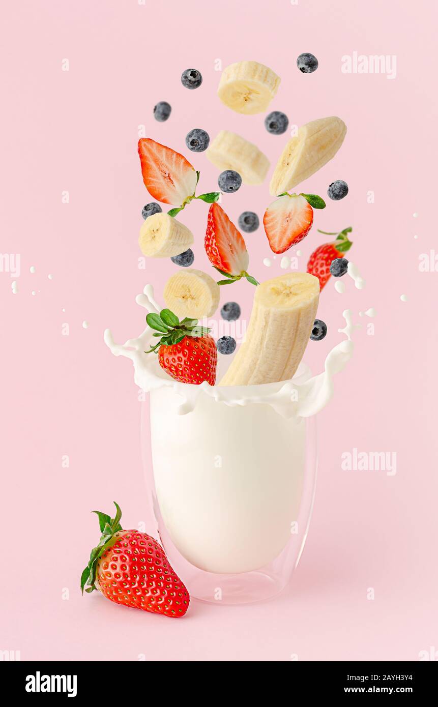 Frische Sommerfrüchte und Beeren fliegen über die spritzende Milch auf pinkfarbenem Hintergrund. Milchshake-Levitation Stockfoto