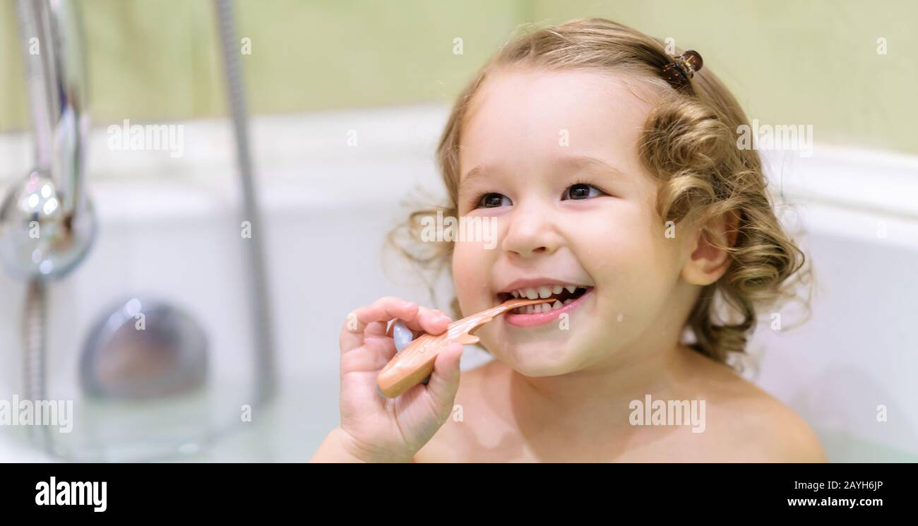 Fröhliches Baby-Mädchen spielt in einem Bad. Zwei Jahre altes schönes Kind beißt einen Spielzeugfisch und lächelt in einer Badewanne. Liebenswerte Kleinkinder beim Baden zu Hause. War Stockfoto