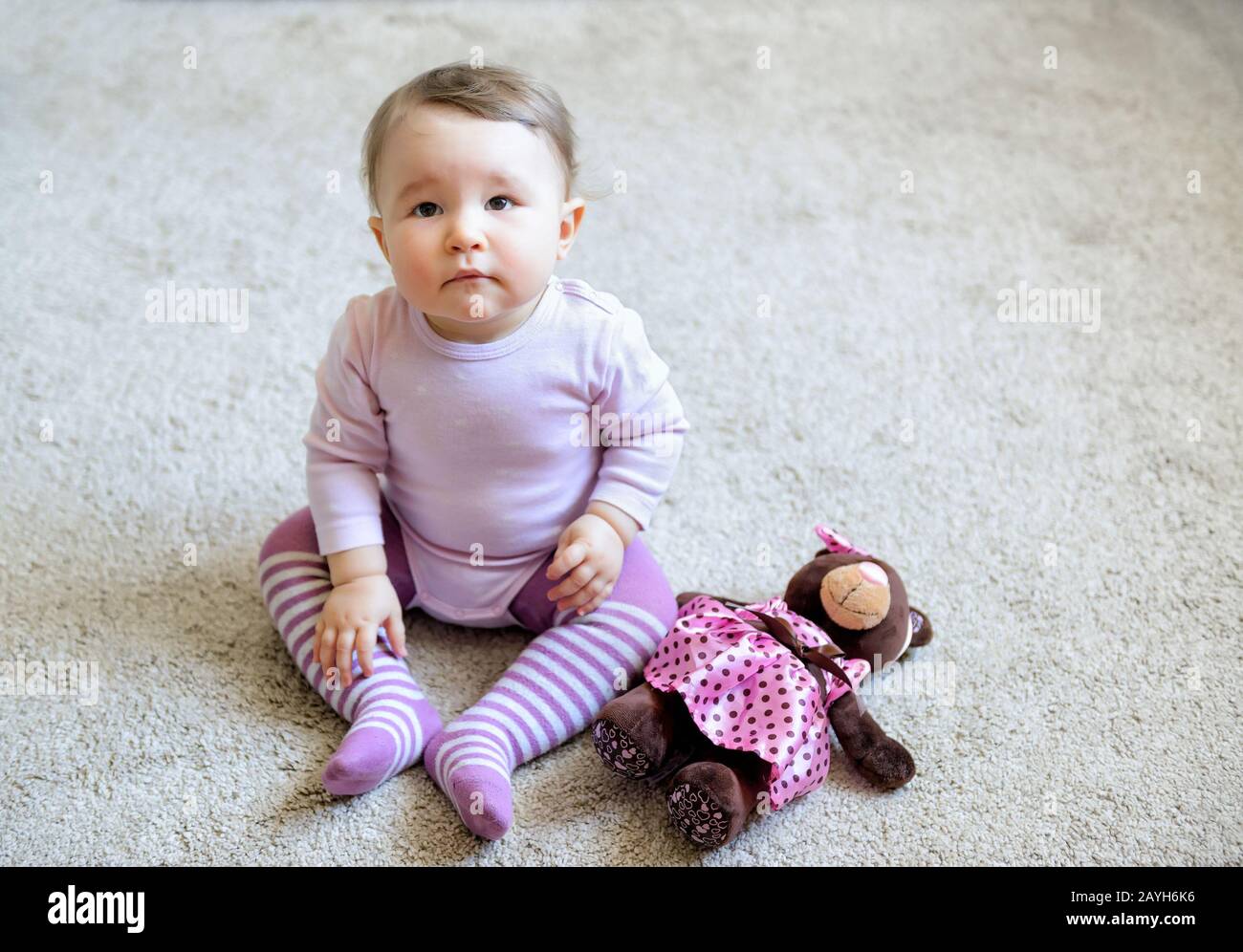 Nachdenkliches und ernsthaftes nettes Mädchen, das zu Hause auf dem Boden sitzt und mit Spielzeugbären trägt Stockfoto