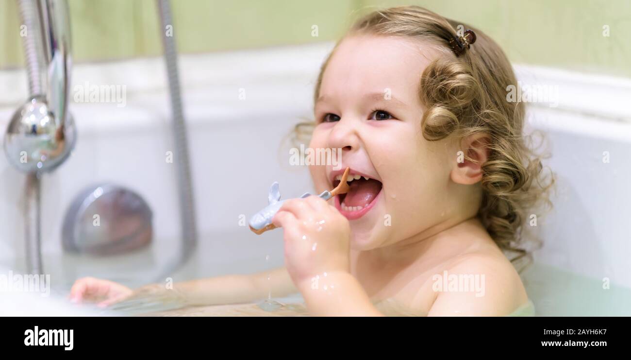 Fröhliches Baby-Mädchen spielt in einem Bad. Das zweijährige Kind hält einen Spielzeugfisch und lacht in einer Badewanne. Lächelnd liebenswürdig kleines Kind beim Baden zu Hause. Waschen Stockfoto
