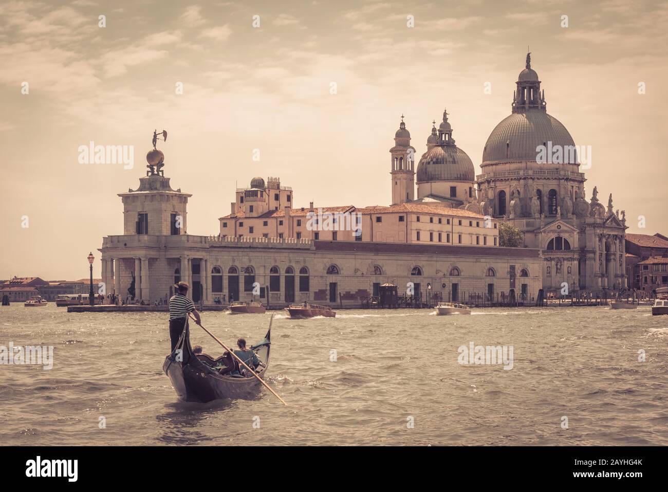 Die Gondel mit Touristen schwimmt entlang des Canal Grande in Venedig, Italien. Santa Maria della Salute Kirche in der Ferne. Die Gondel ist die attraktivste Stockfoto