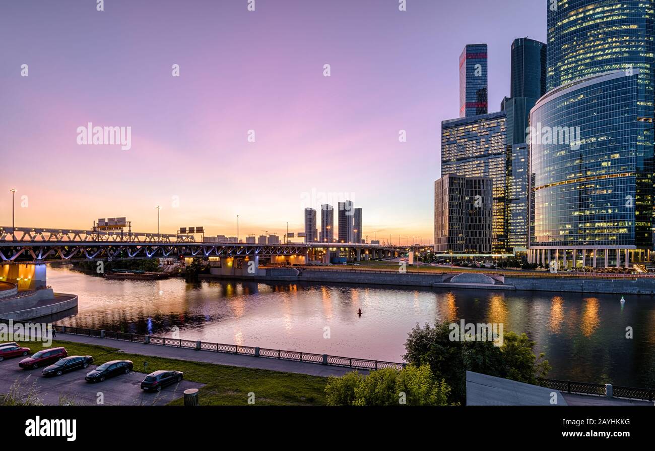 Blick auf den Moskva-Fluss mit Wolkenkratzern und Brücke in der Nacht, Moskau, Russland. Moderne Gebäude im Hintergrund des Sonnenhimmels. Blick auf die Moskau-Ci am Abend Stockfoto
