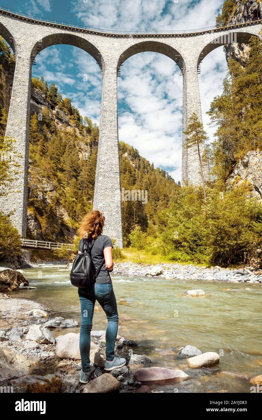 Landwasser-Viadukt in Filisur, Schweiz. Junge hübsche Frau blickt auf die berühmte Touristenattraktion. Wunderschöner Blick auf die hohe Eisenbahnbrücke in m Stockfoto