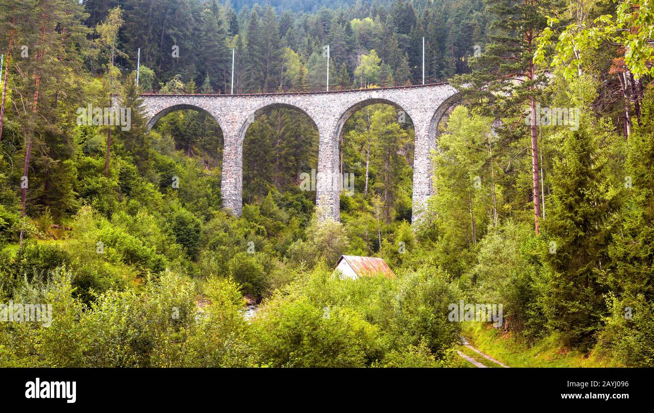 Landschaft mit Hochbrücke und kleinem Haus, Filisur, Schweiz. Panorama Alpenwald. Schöne Aussicht auf das Viadukt im Sommer. Berglandschaft mit Stockfoto