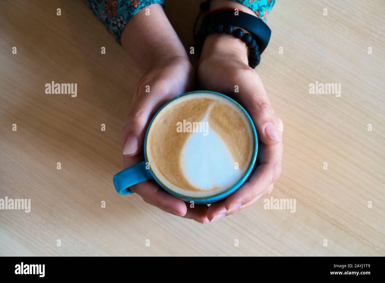 Weibliche Hände umarmen einen großen Becher mit Cappuccino. Stockfoto