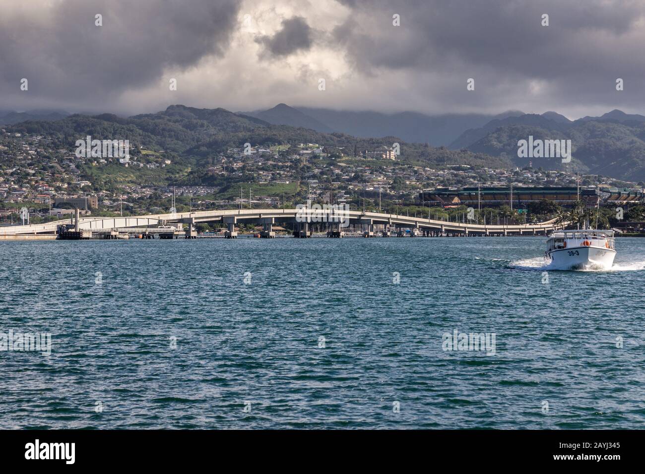 Oahu, Hawaii, USA. - 10. Januar 2012: Pearl Harbor. Die Brücke von Ford Island schäumt weiße Linien zwischen blauem Wasser und einem Gürtel grüner Hügel mit weißem Haus Stockfoto