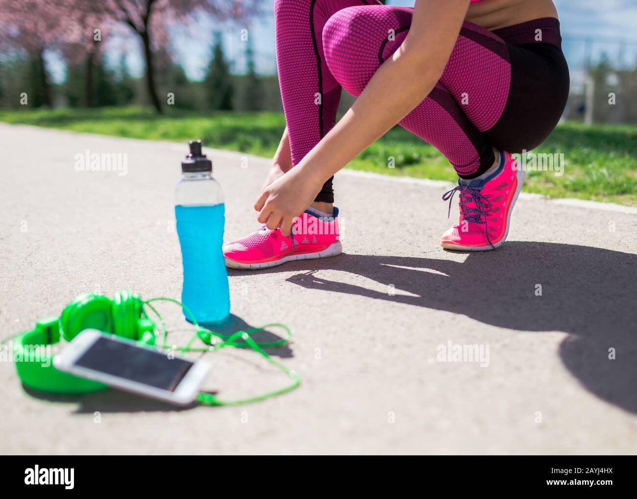 Junge Fitness-Mädchen, die Schuhe binden, bevor sie laufen. Weibliche Läuferin mit Energydrink und Kopfhörer auf der Strecke. Sportangebot. Gesundes li Stockfoto