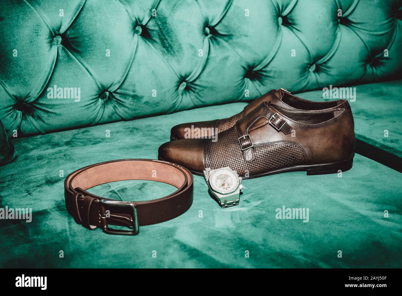 Braune Herrenschuhe mit Gürtel und Armbanduhr auf grünem Sofa Stockfoto