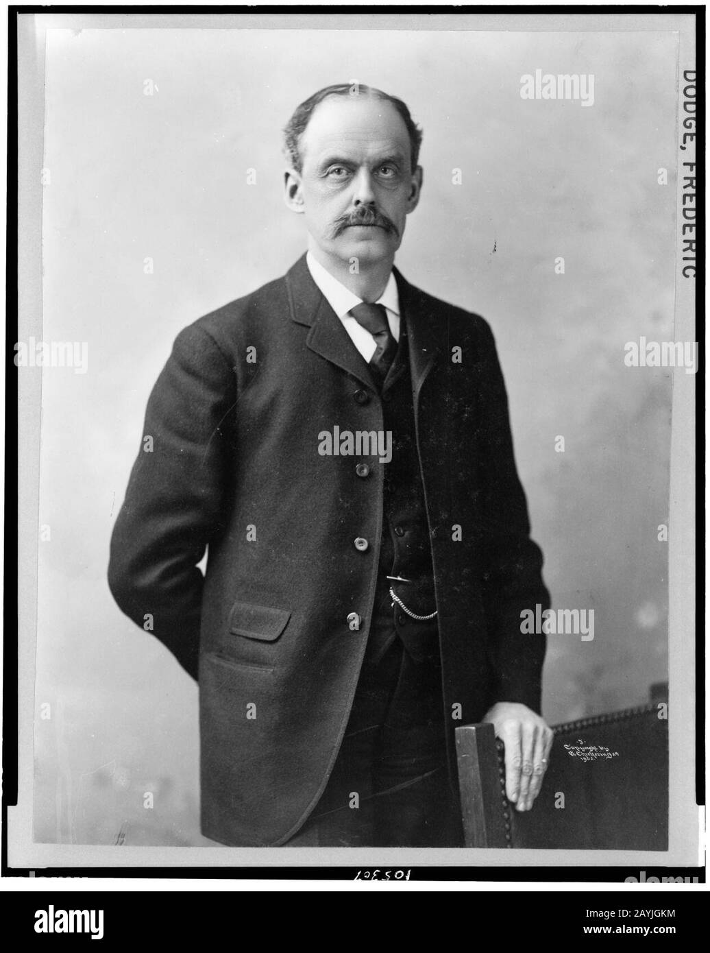 Frederic Dodge, halb langes Porträt, leicht nach rechts gerichtet, linke Hand auf der Rückseite des Stuhls Stockfoto