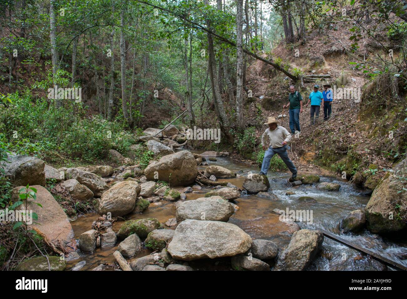 Menschen, die einen Bach in der Nähe der Wasserfälle in den Hügeln oberhalb des mixtekischen Dorfes San Juan Contreras in der Nähe von Oaxaca, Mexiko, überqueren. Stockfoto