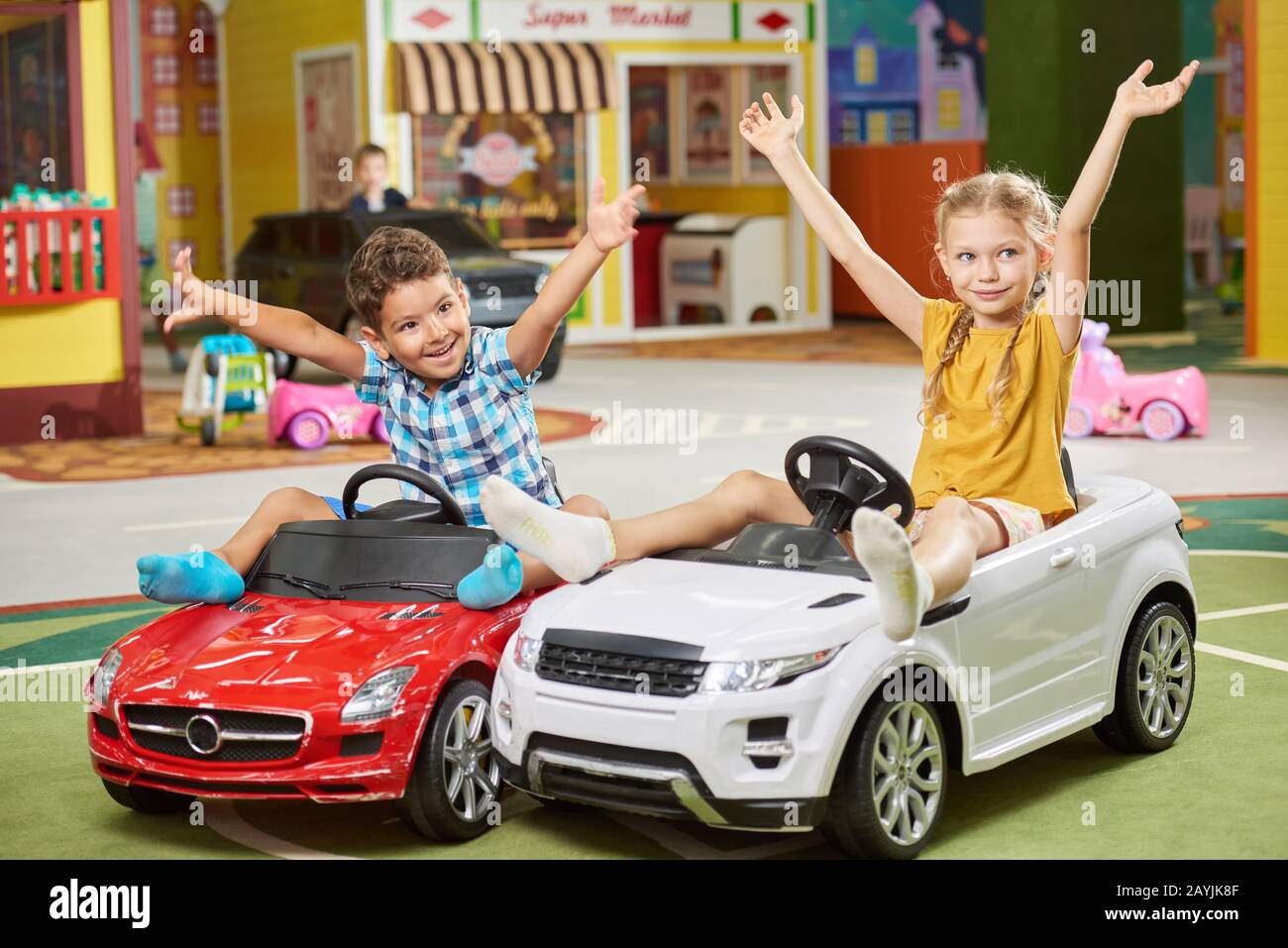 Glückliche Kinder sitzen in Spielzeugautos im Kindergarten. Stockfoto