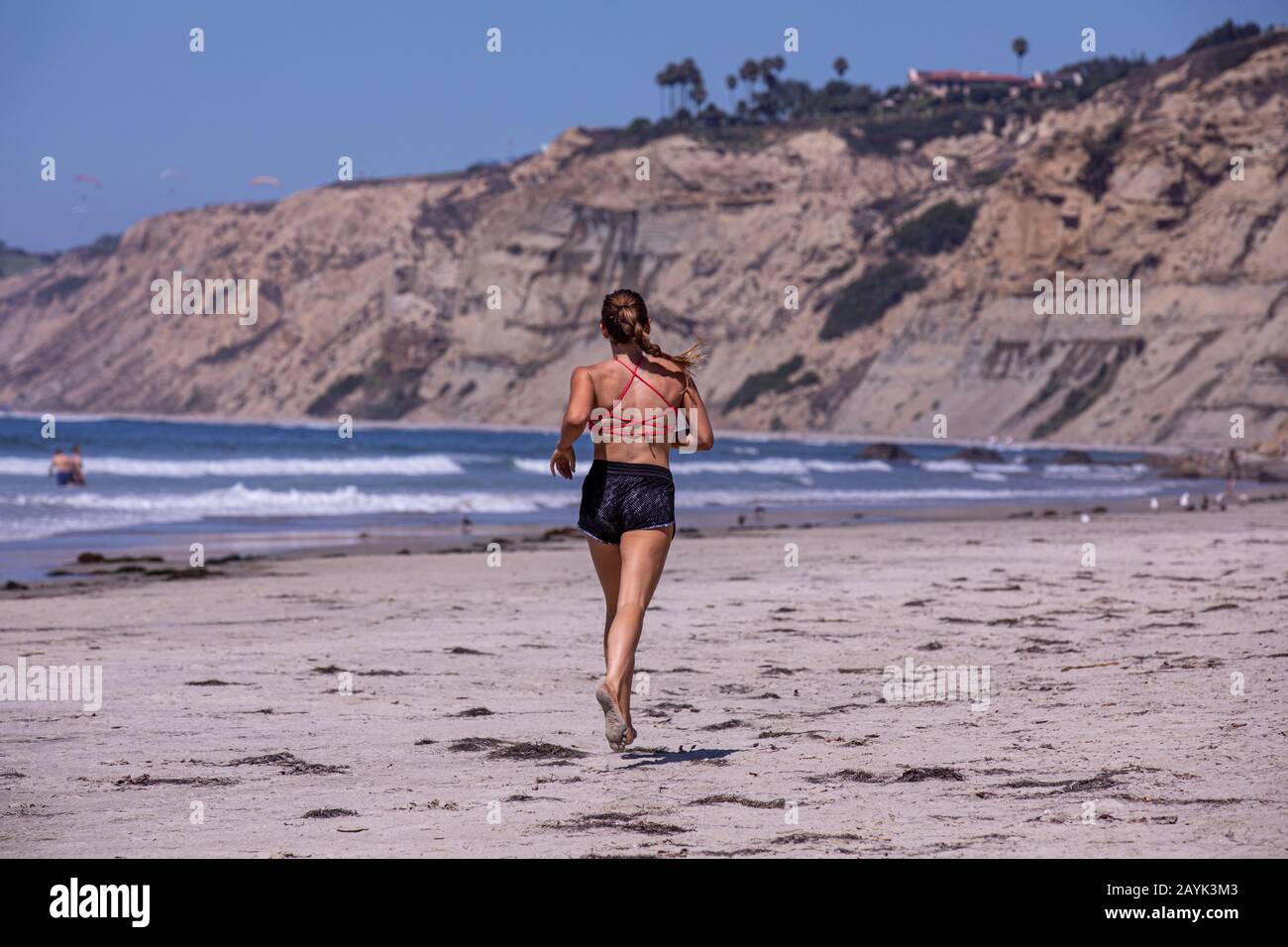 Eine junge Frau, die barfuß an einem Scripps Strand, San Diego, Kalifornien, joggt Stockfoto