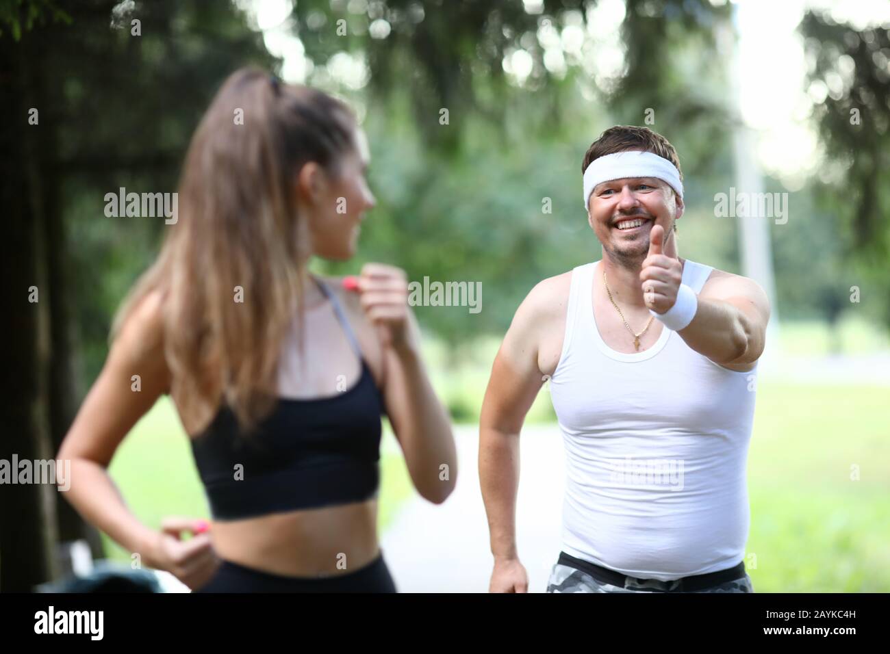 Der Mann im Park zeigt dem Sportmädchen eine Geste. Stockfoto