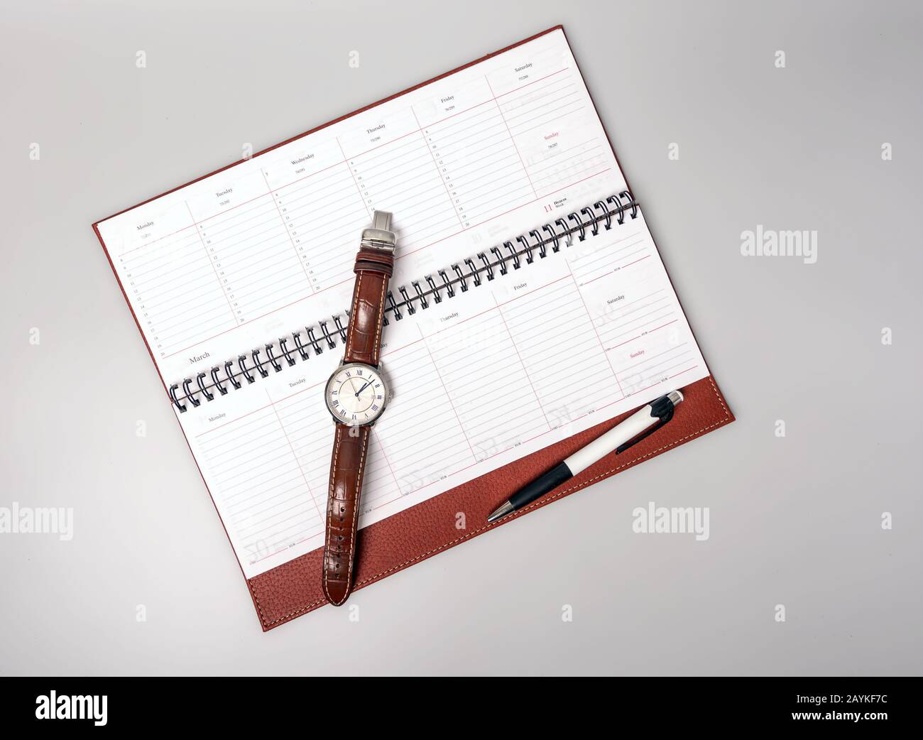 Geschlossenes Notebook in Lederbindung mit Stift und Uhr auf grauem Hintergrund. Platz für Text. Stockfoto