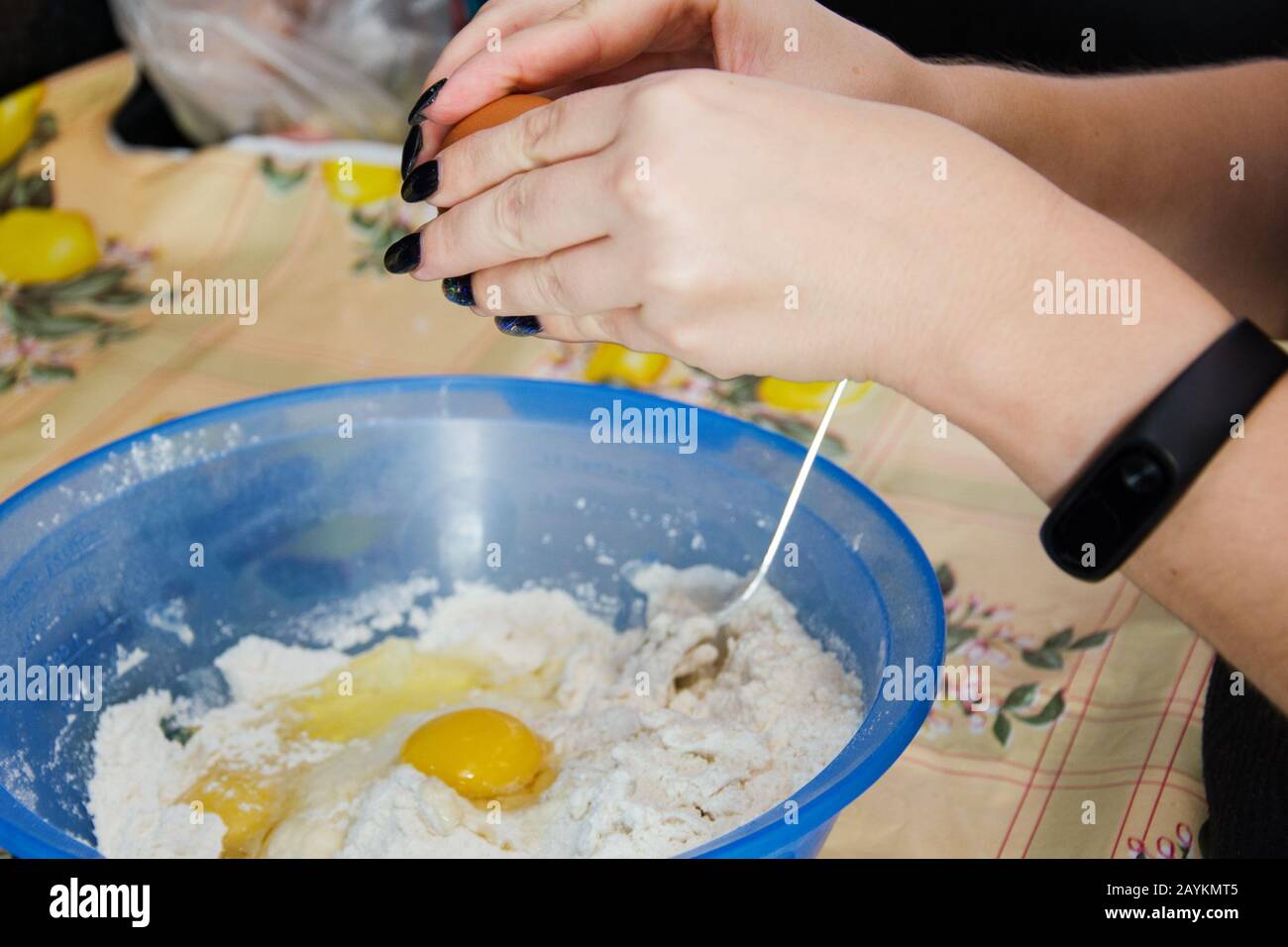 Frau mit schwarzer Maniküre und Eier in eine blaue Schüssel Mehl zerbrechen, um Teig zu machen. Stockfoto