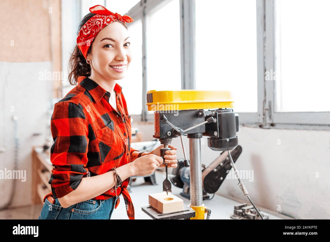 Eine starke und unabhängige Asiatin arbeitet an einer Bohrmaschine in einer Fabrik oder Werkstatt. Konzept mit blauem Kragen Stockfoto