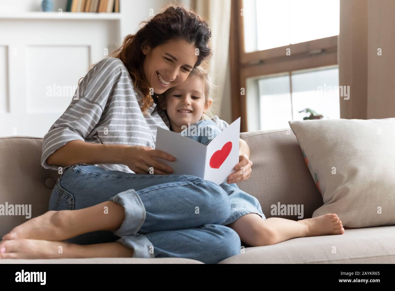Fröhliche junge lockige Mutter, die Glückwünsche auf Karte liest. Stockfoto