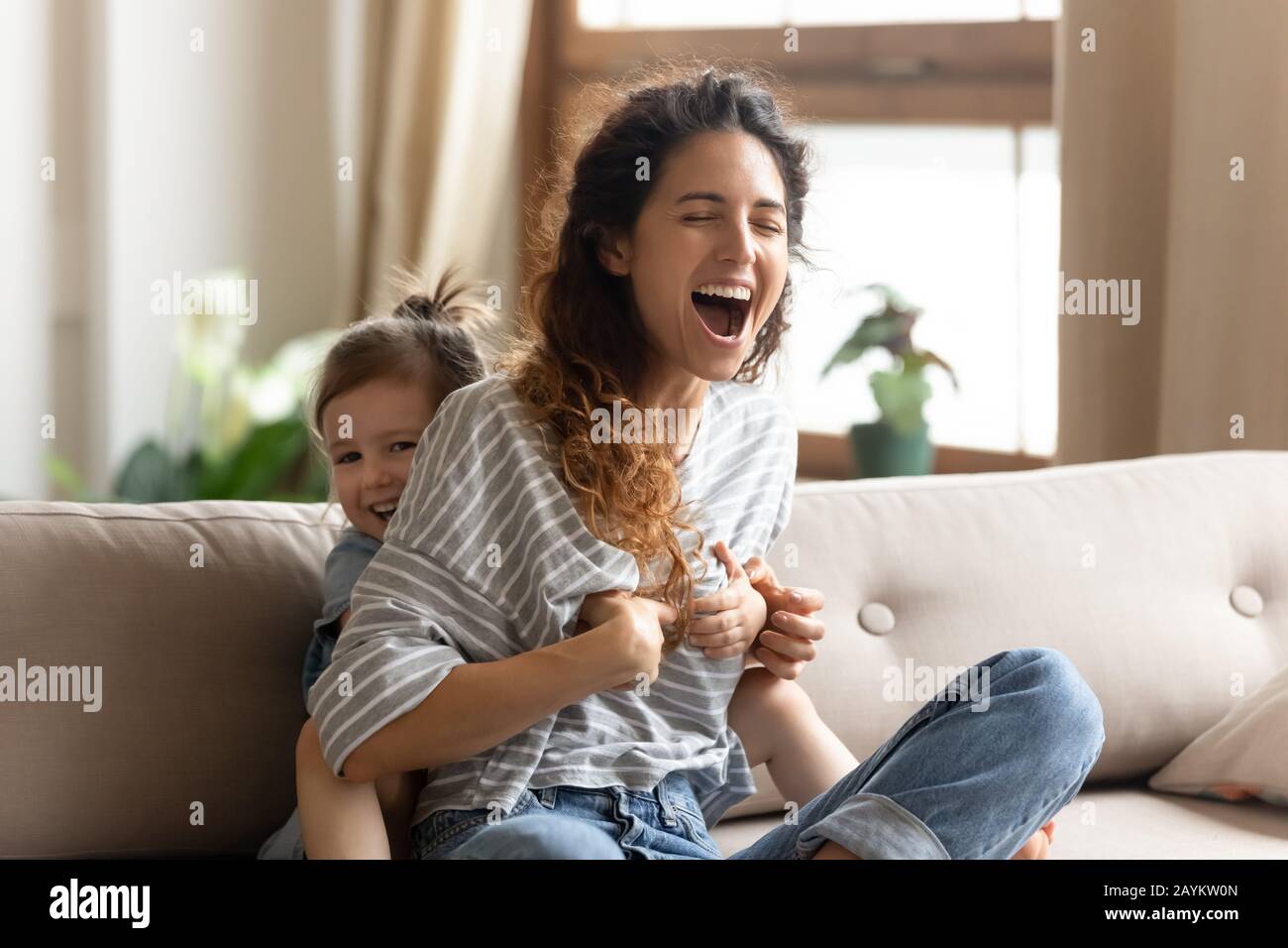 Verspieltes kleines Kindermädchen kitzelt lachende Frau. Stockfoto