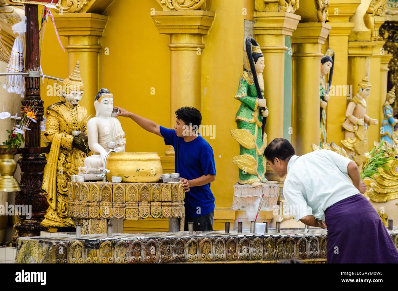 Der Anhänger gießt Wasser über die Buddha-Statue und bietet Räucherstäbchen an einem Planetenposten, Myanmar Stockfoto