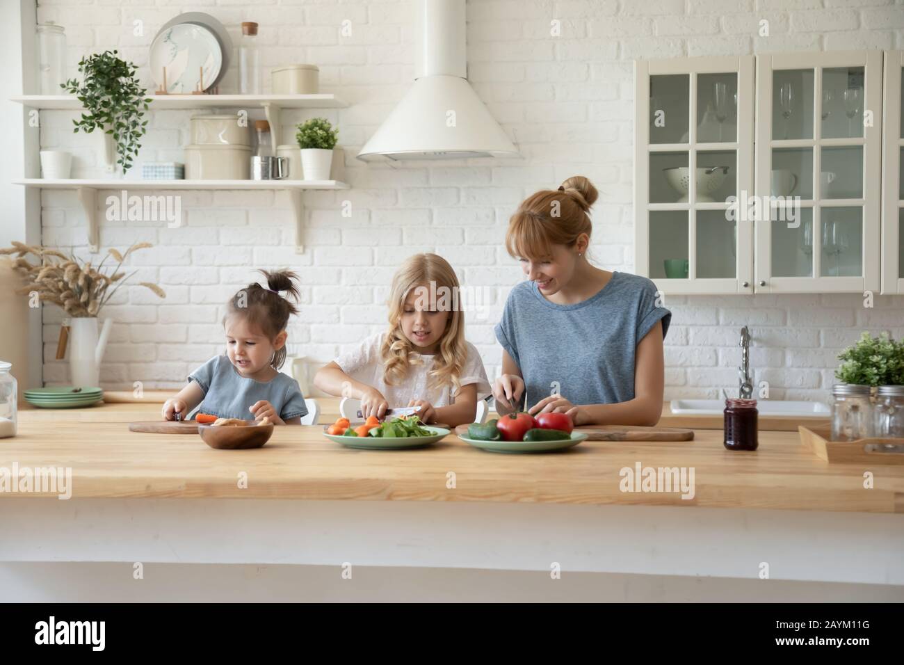 Fürsorgliche Mama, die zusammen mit kleinen Töchtern kocht Stockfoto