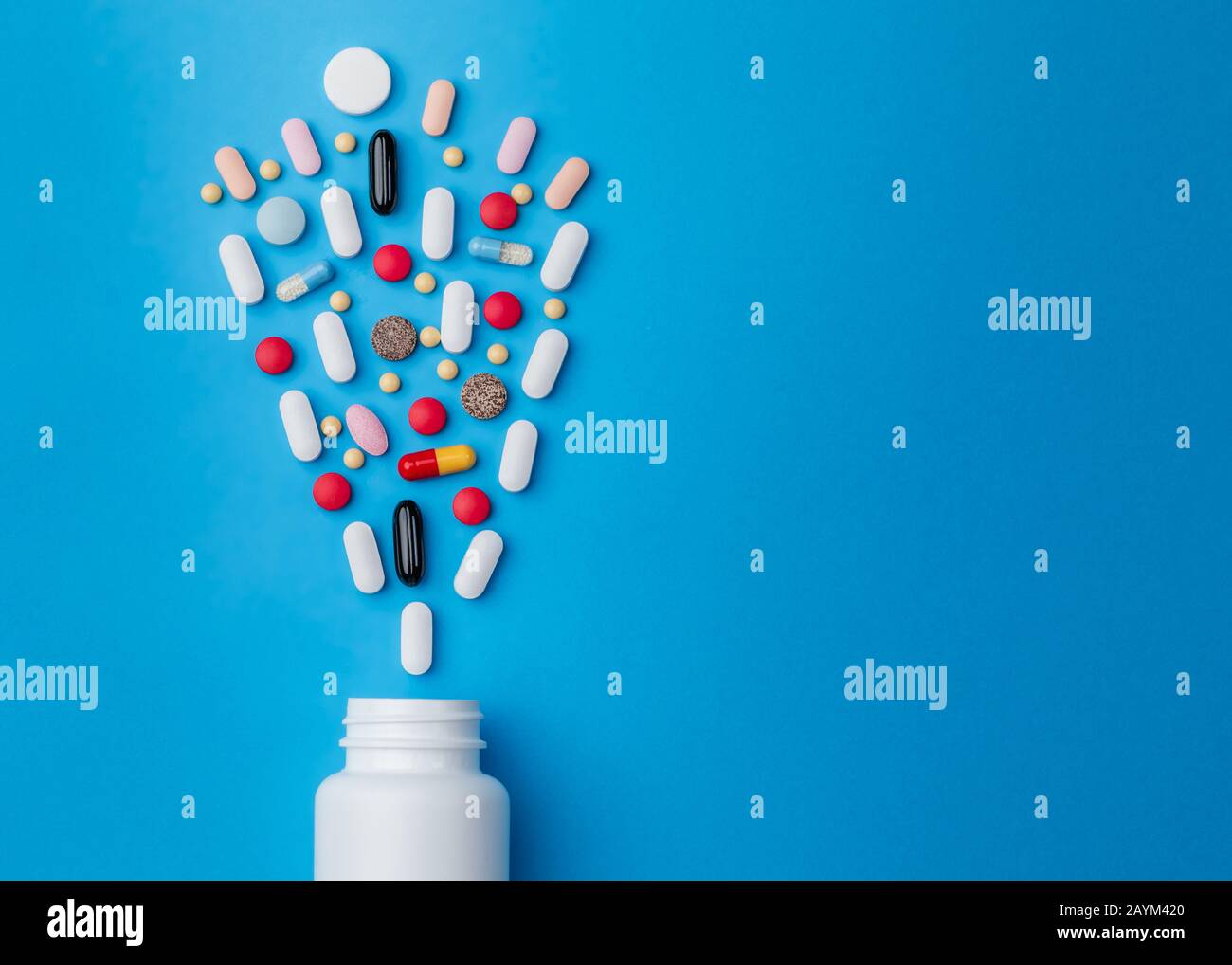 Bunte Pillen aus weißer Flasche auf blauem Hintergrund. Pharmazie und Medizinkonzept. Stockfoto