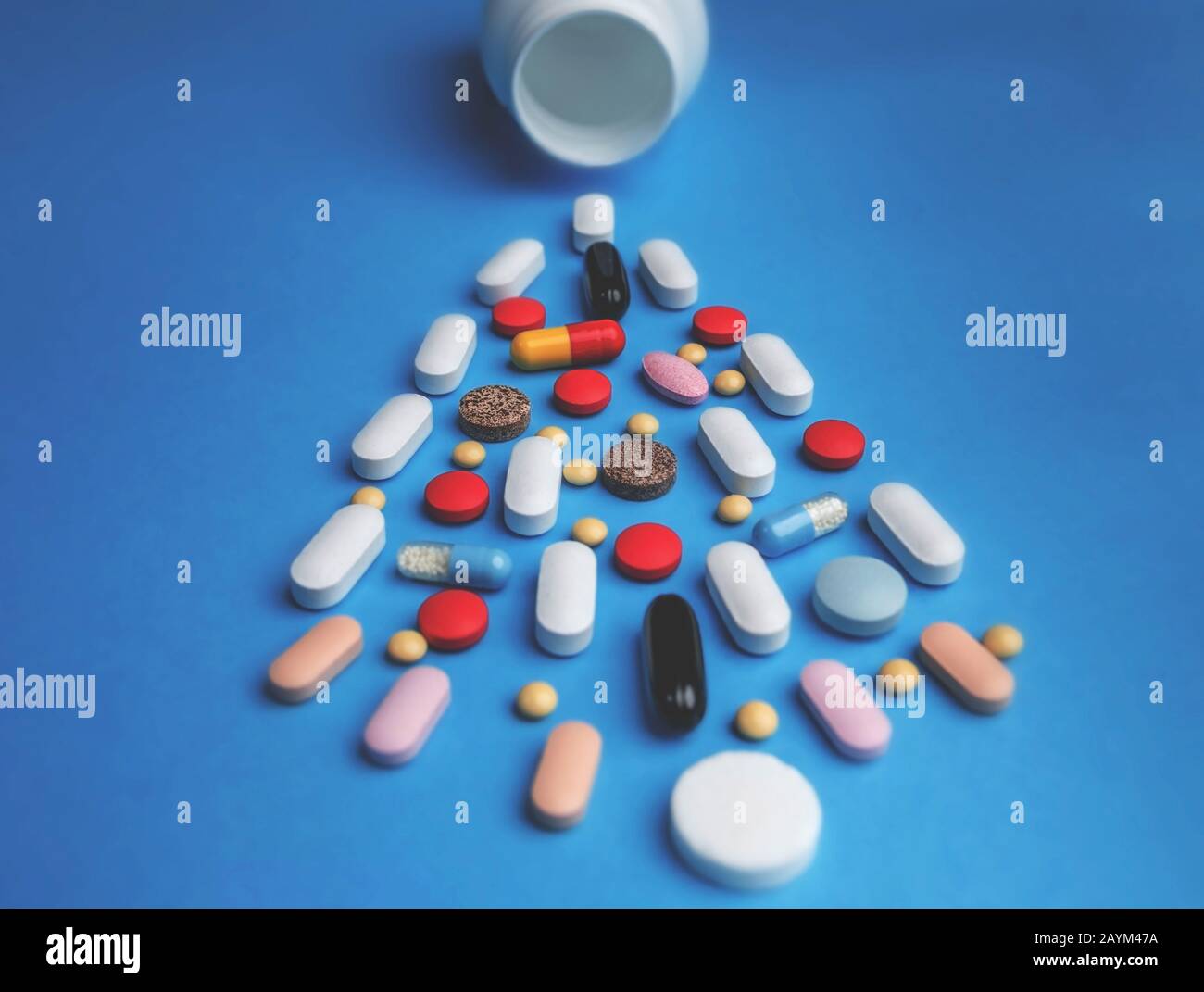 Bunte Pillen aus weißer Flasche auf blauem Hintergrund. Pharmazie und Medizinkonzept. Stockfoto