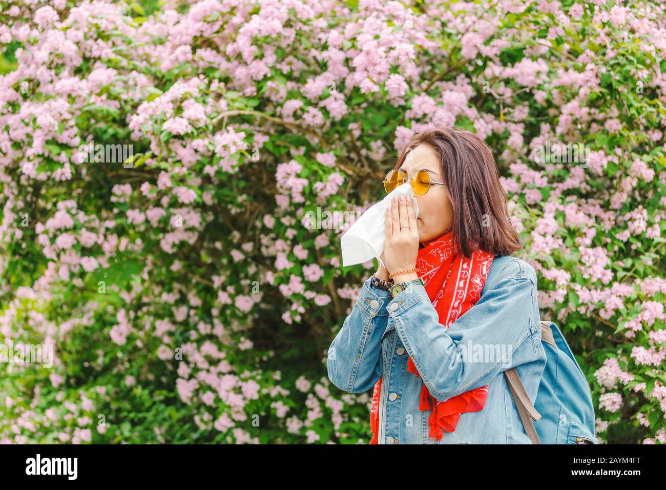 Allergiekonzept. Junge asiatin niest und bläst ihre Nase mit einem Taschentuch und leidet im Frühjahr unter blühenden und blühenden Bäumen. Stockfoto