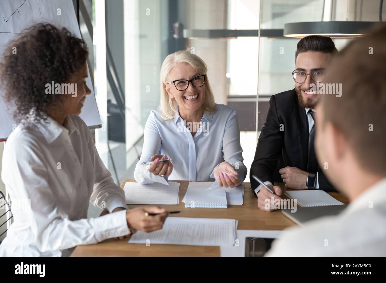 Multiethnische, lächelnde Büroangestellte plaudern bei Briefing im Sitzungssaal Stockfoto