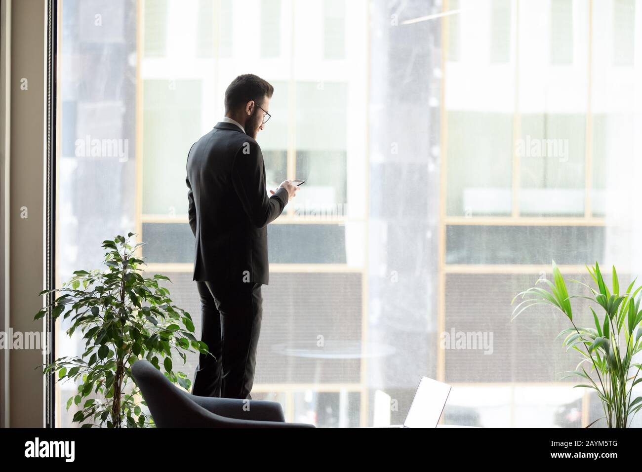Geschäftsmann aus dem mittleren Osten, der in der Nähe eines Panoramafensters mit Smartphone steht Stockfoto