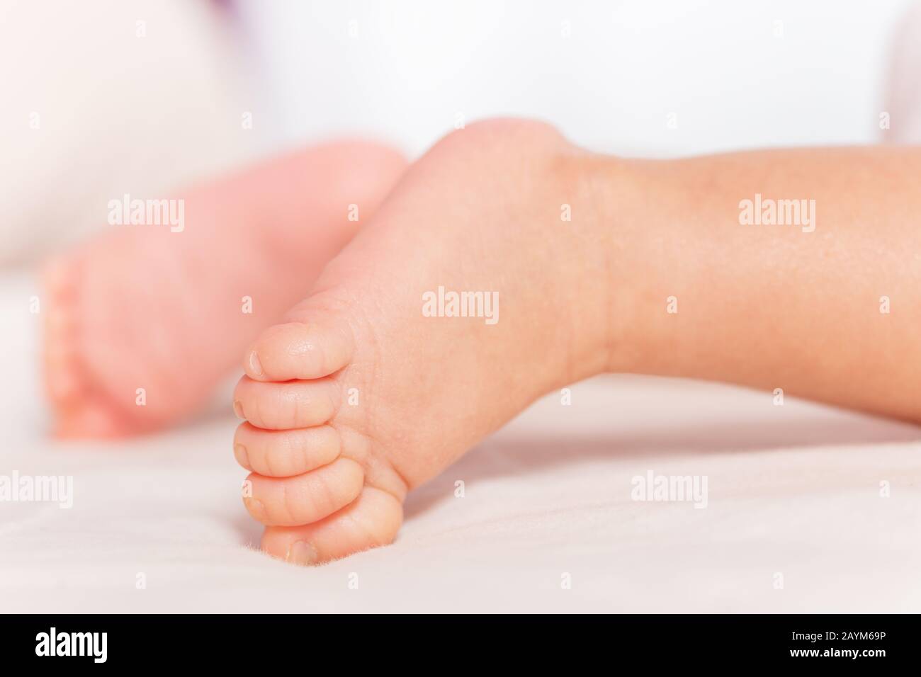 Füße nah oben von neugeborenem Säuglingsjungen, der auf dem Betttuch liegt Stockfoto