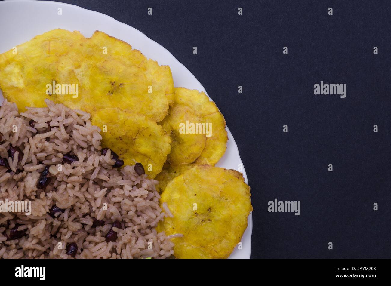 Nahaufnahme der weißen Platte mit Congris Reis traditionelle kubanische Küche mit gebratenen Pataconen. Auch bekannt als gallo Pinto mit Steinen. Stockfoto