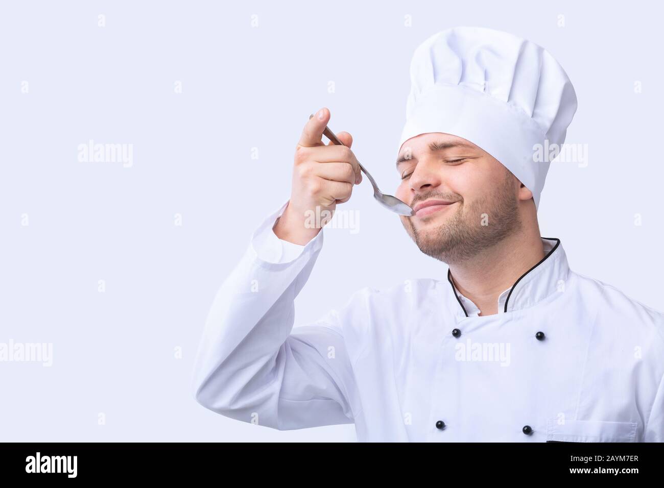 Küchenchef Tasting Food Holding Spoon Standing, Studio Shot Stockfoto