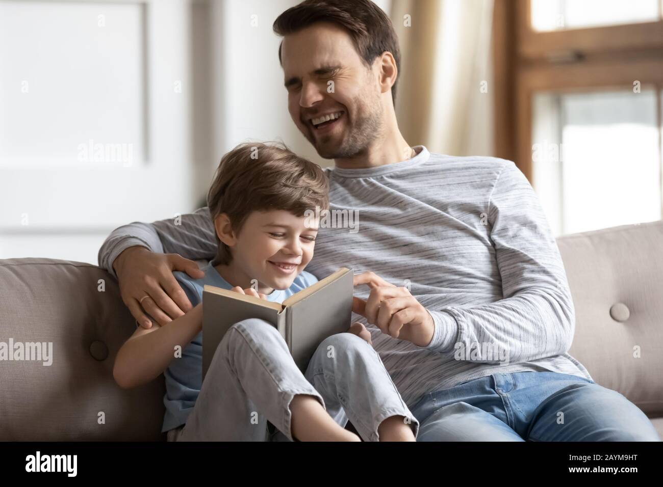 Fröhlicher kleiner Junge lacht über die Geschichte und liest Buch mit dem Vater. Stockfoto