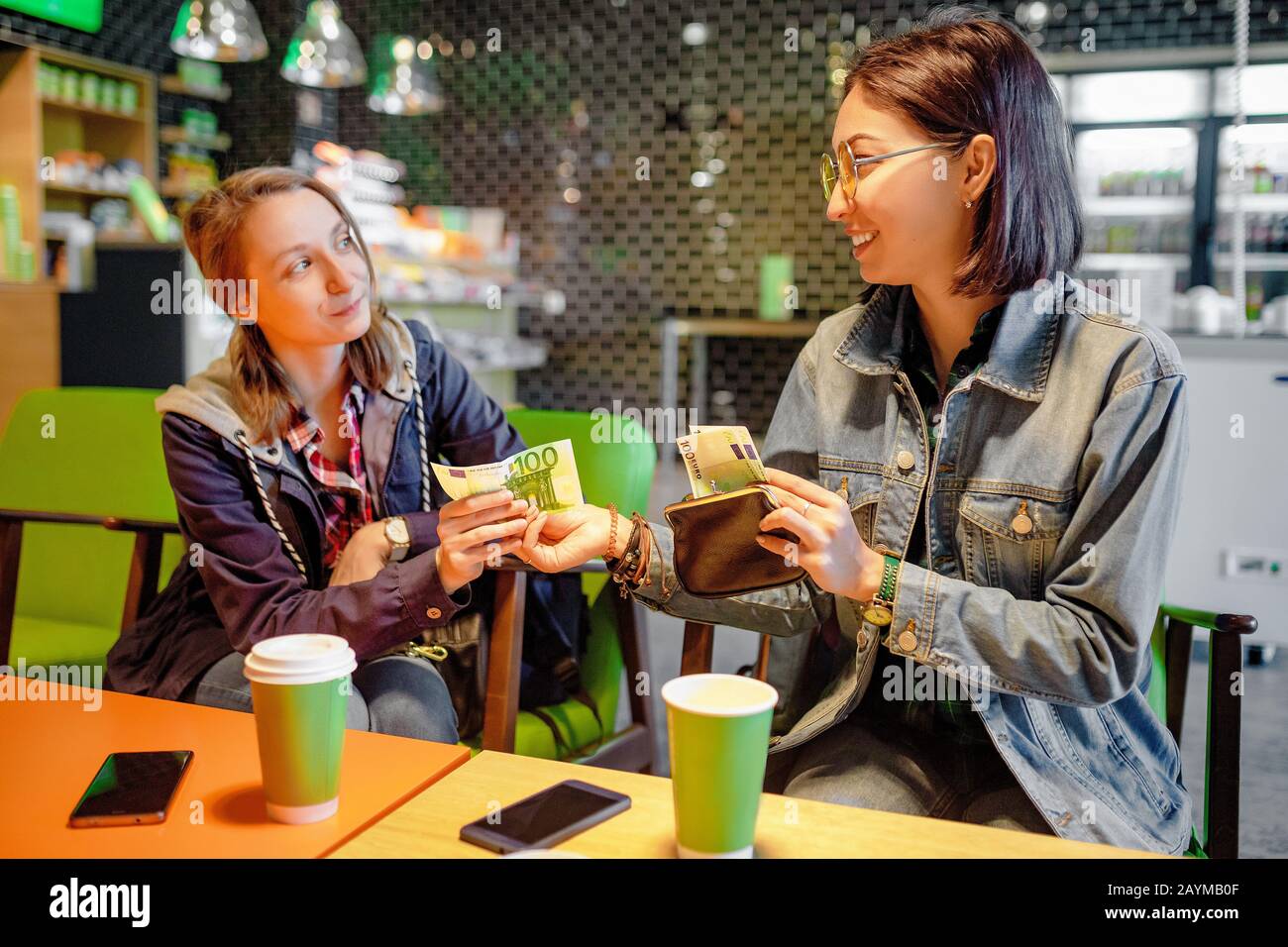 Eine Frau gibt einer fremden Person oder ihrem Freund im Inneren eines Cafés Euro-Banknotengeld. Das Konzept des Geldverleihens oder Betrugs Stockfoto