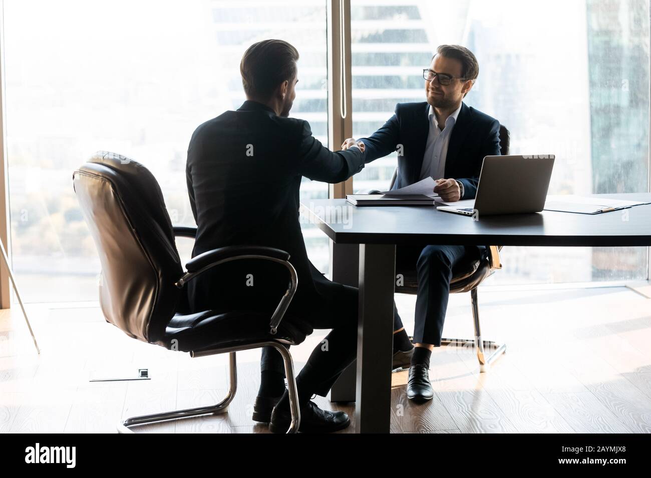 Glücklicher bärtiger Geschäftsmann im Anzug schüttelt mit Arbeitssuchenden die Hände. Stockfoto