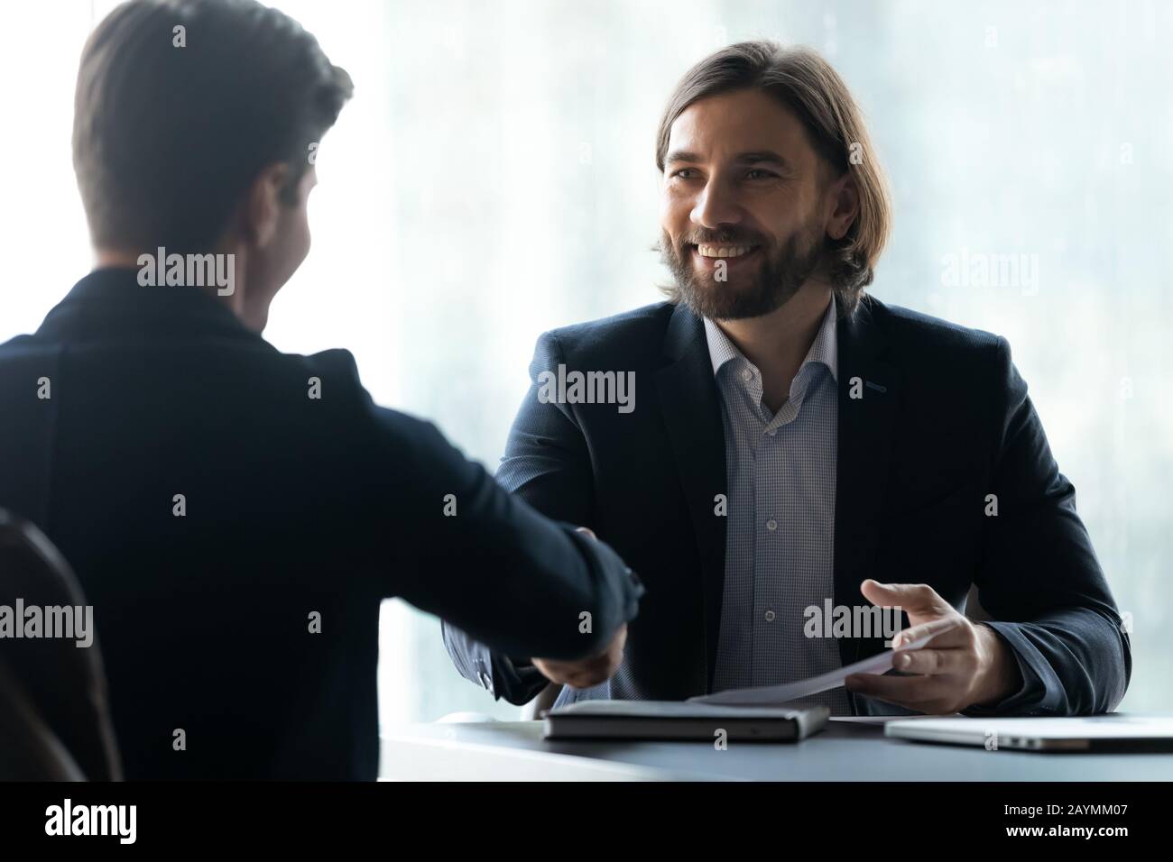 Lächelnder Geschäftsmann im Anzug schüttelt mit Arbeitssuchenden die Hände. Stockfoto