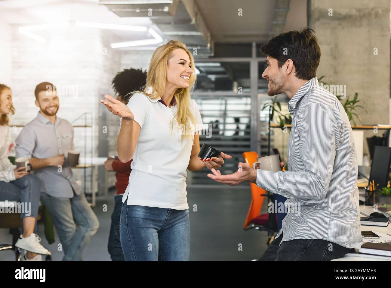 Junge, freundliche Kollegen, die am Arbeitsplatz Gespräche führen Stockfoto