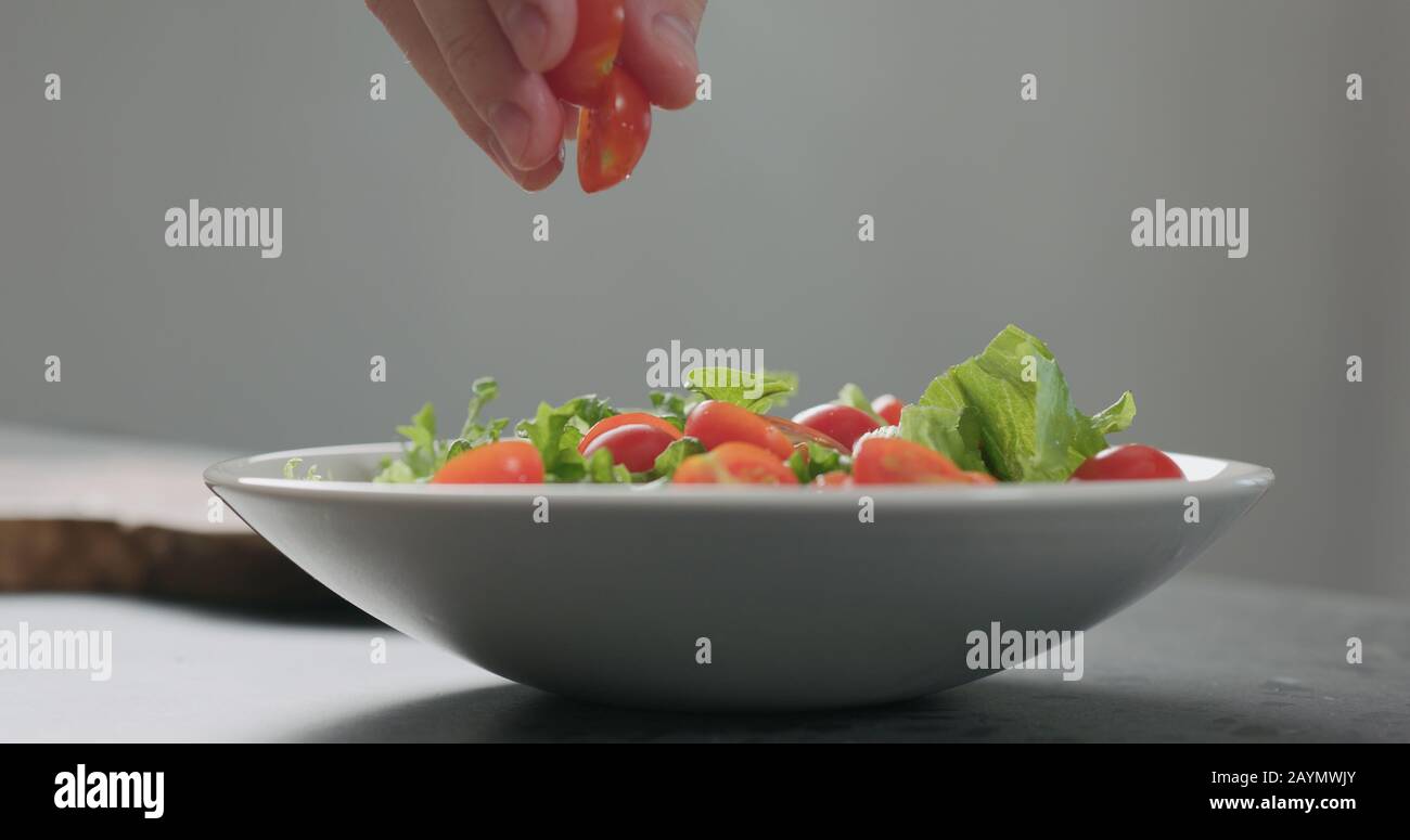 Fügen Sie Kirschtomaten und Friseeblätter in eine weiße Schüssel, ein breites Foto Stockfoto