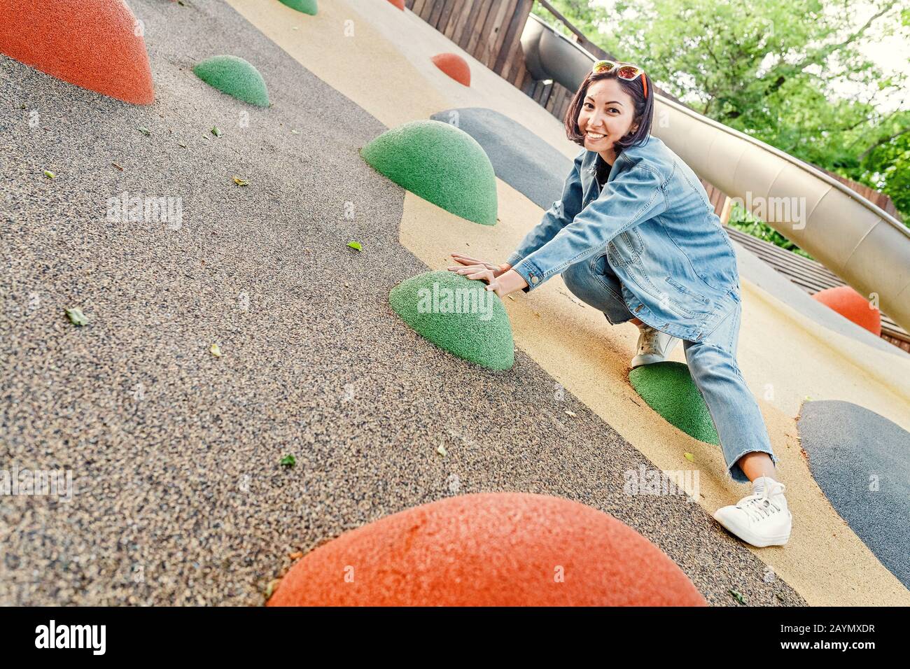 Fröhliche Frau klettert auf einem städtischen Spielplatz an einer Wand Stockfoto