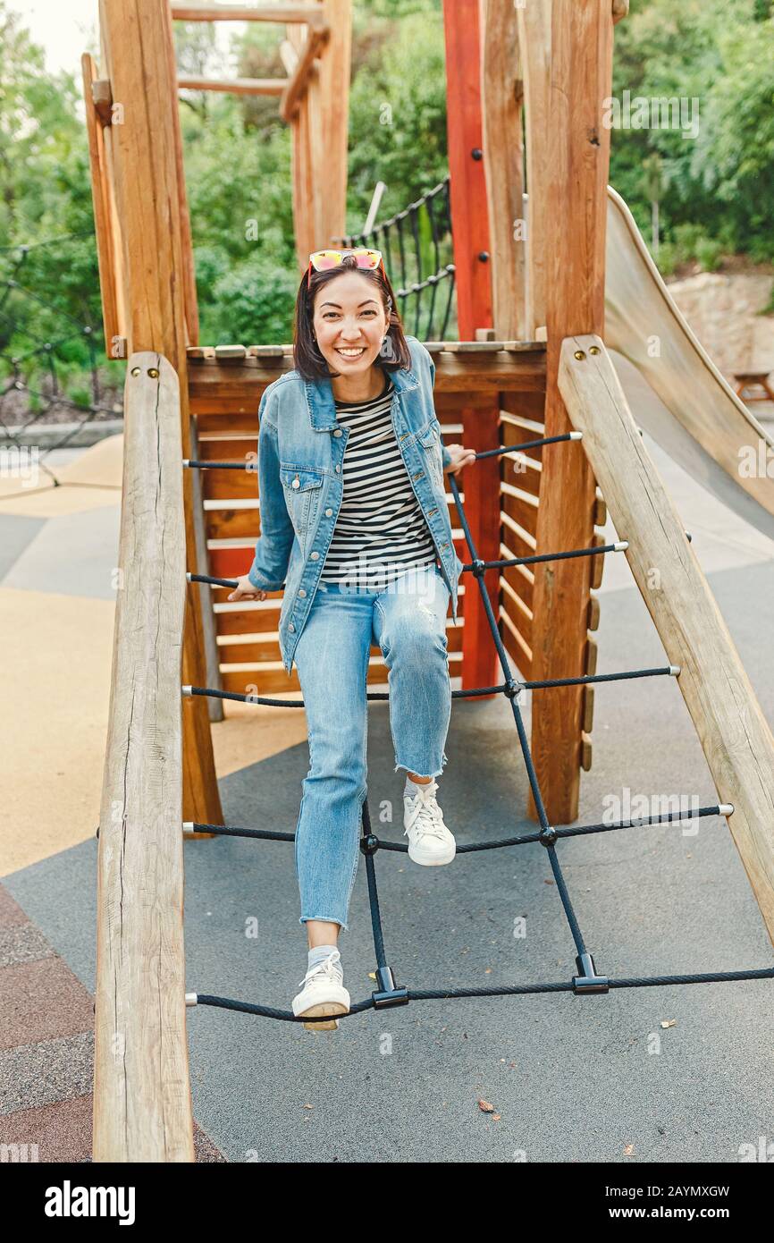 Eine infantile und glückliche Frau, die auf einer Kinderrutsche auf einem Spielplatz sitzt Stockfoto