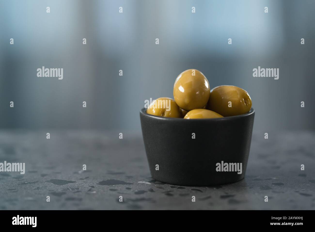 Ganze große grüne Oliven in kleiner schwarzer Schüssel auf Betongrund, flacher Fokus Stockfoto