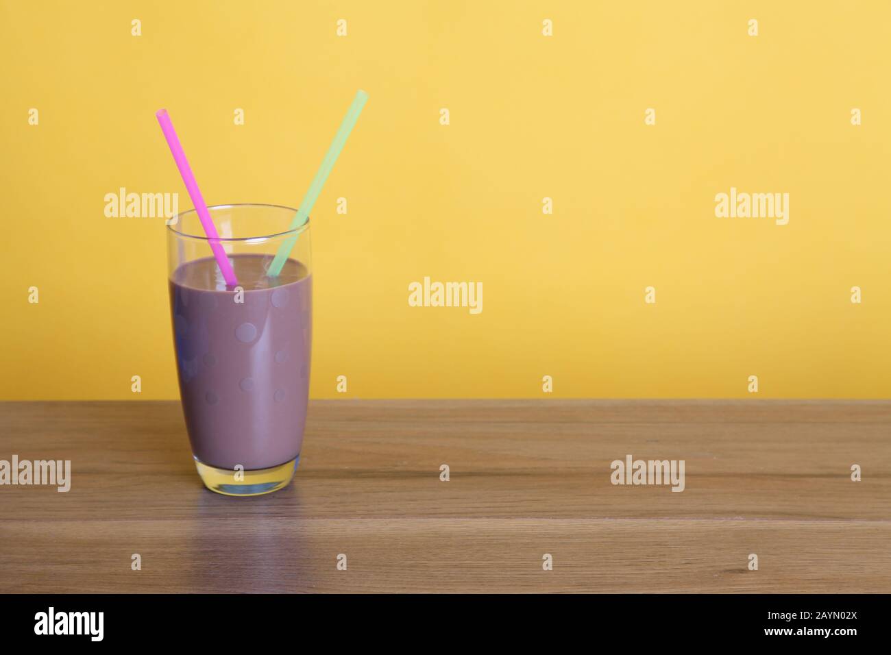 Ein halbes Pint Glas Schokoladenmilch mit zwei Strohhalmen auf Holztisch mit Copyspace auf gelbem Hintergrund Stockfoto