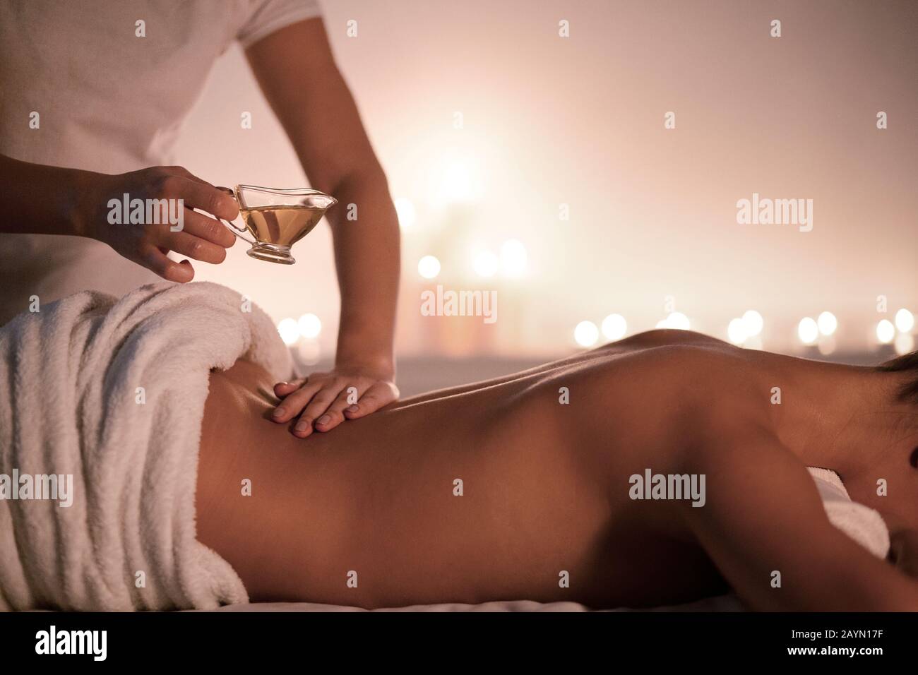 Entspannende Spa-Massage. Masseur gießt Öl auf den weiblichen Rücken Stockfoto