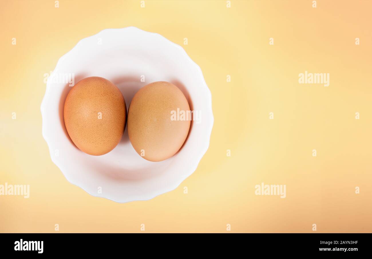 Ein Paar braune Eier in weißer Schüssel auf pastellgelbem Hintergrund mit Copyspace. Beschneidungspfad für einfaches Ausschneiden zum Ersetzen des Hintergrunds Stockfoto